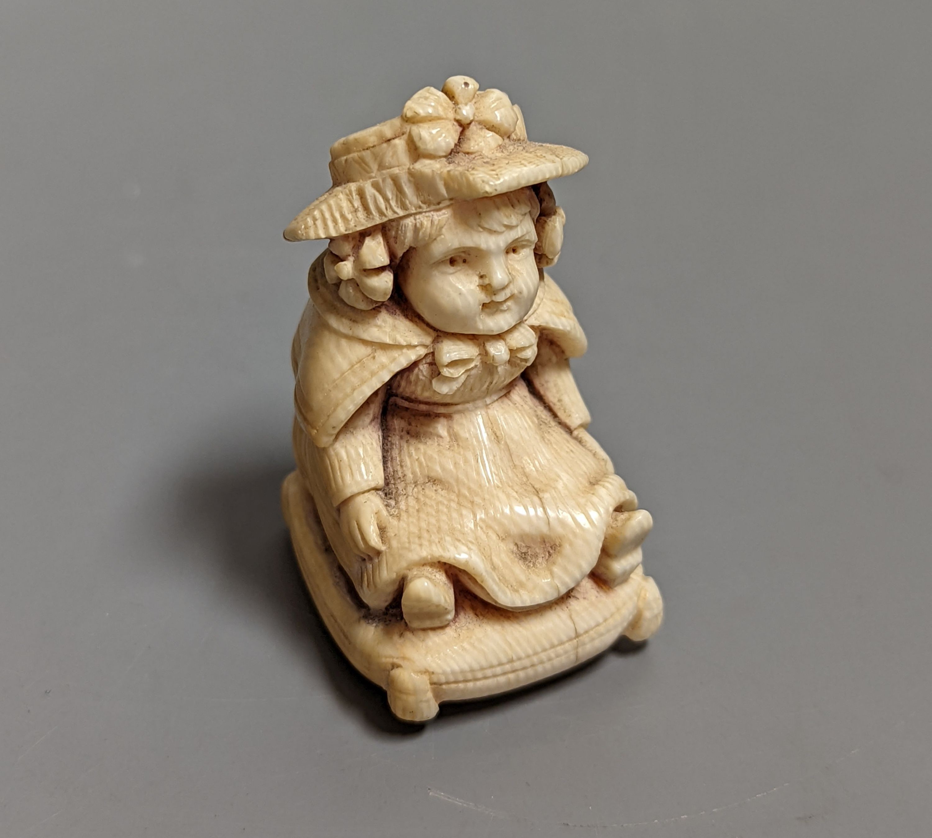 A late 19th/early 20th century carving of a girl seated on a cushion, 5 cms high